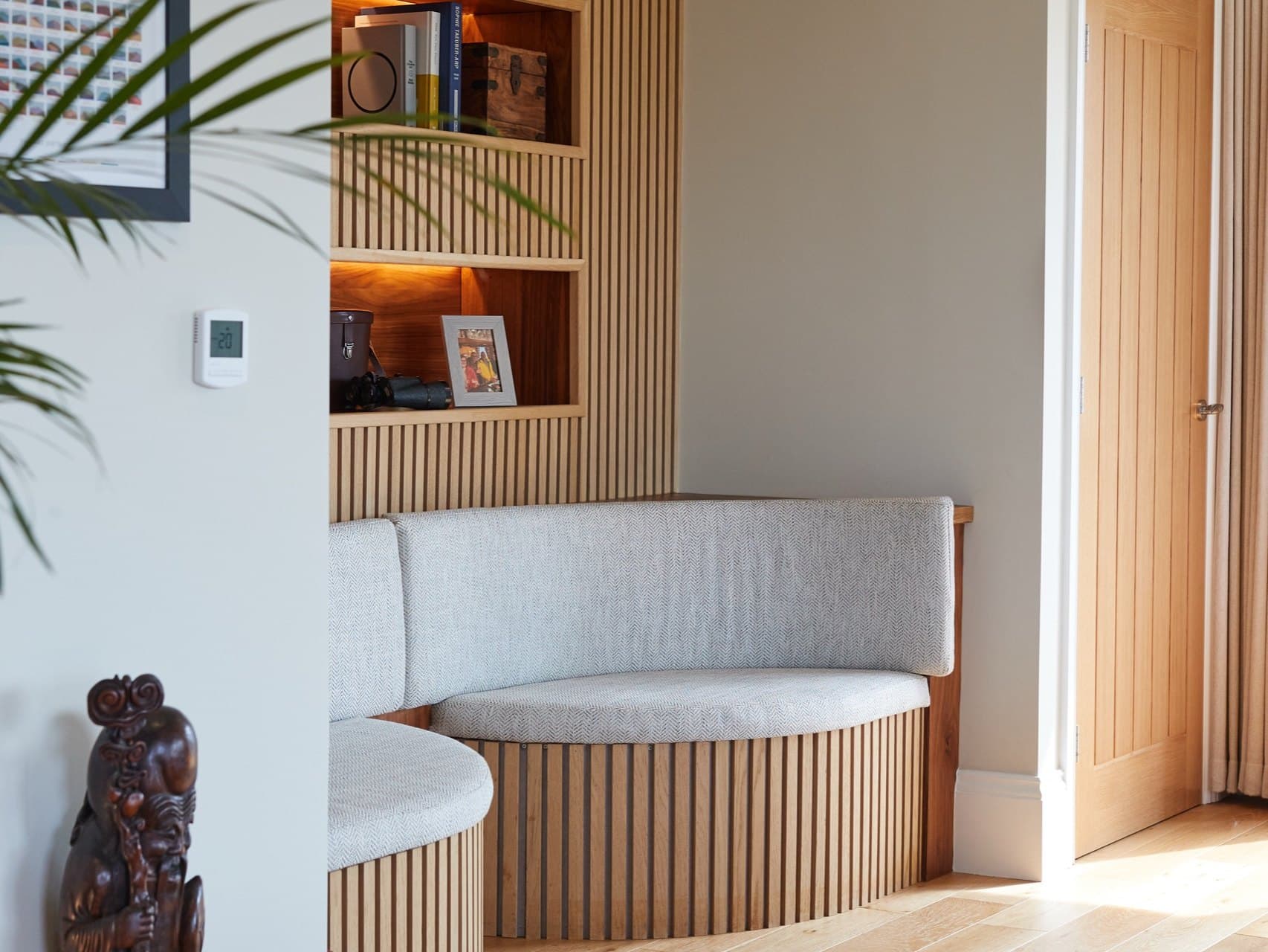 A curved oak-slatted banquette set into a panelled recess, beside lit oak shelving — crafted joinery at Kiln Heights